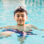 A brown-haried boy in a pool, smiling
