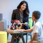 A female therapist talking to a boy playing with blocks